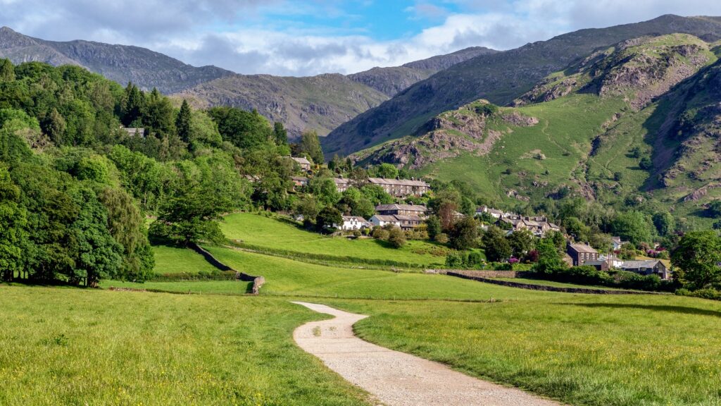 Où dormir dans le Lake District ? Les 5 meilleurs quartiers et hébergements 22 Chemin à travers un pré herbeux en direction du village de Coniston, avec des collines à l’arrière-plan