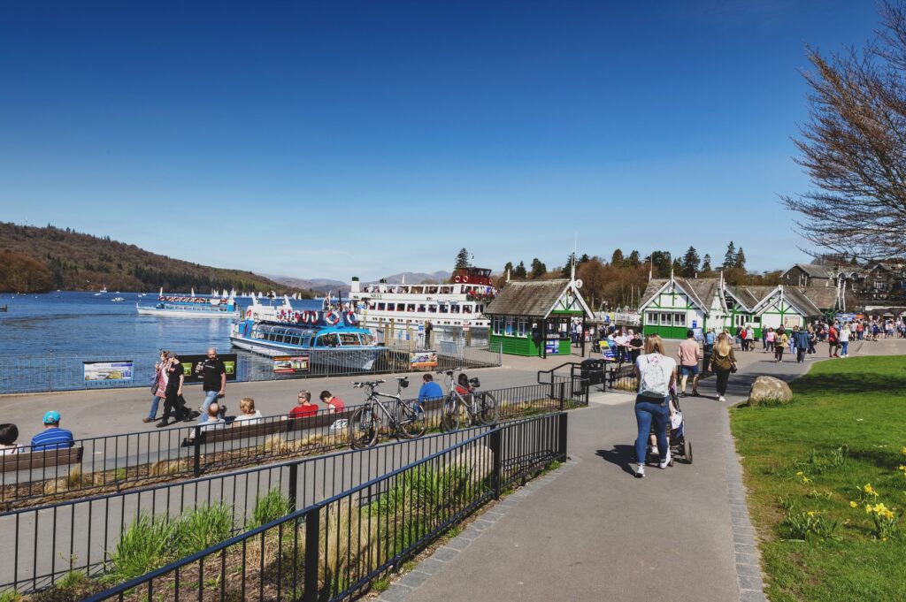 Où dormir dans le Lake District ? Les 5 meilleurs quartiers et hébergements 14 Des promeneurs sur le front de lac de Bowness-on-Windermere, avec un bateau sur l’eau